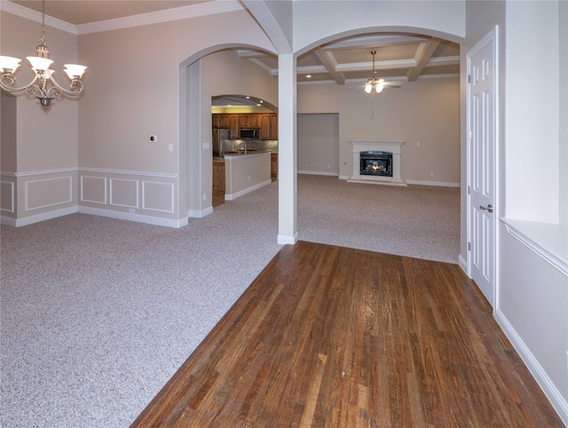 unfurnished dining area with arched walkways, coffered ceiling, a glass covered fireplace, and ceiling fan with notable chandelier