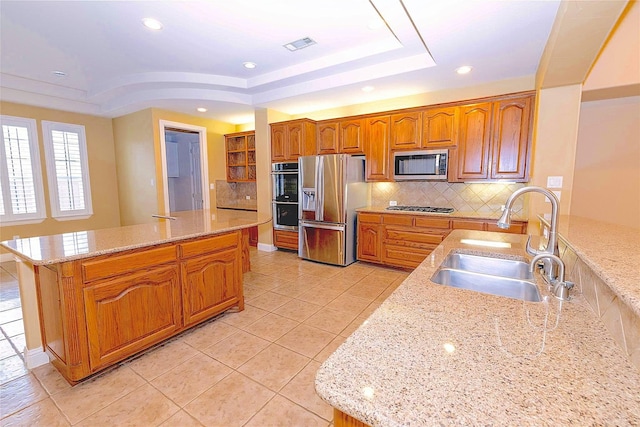 kitchen featuring brown cabinets, tasteful backsplash, light stone counters, a sink, and appliances with stainless steel finishes
