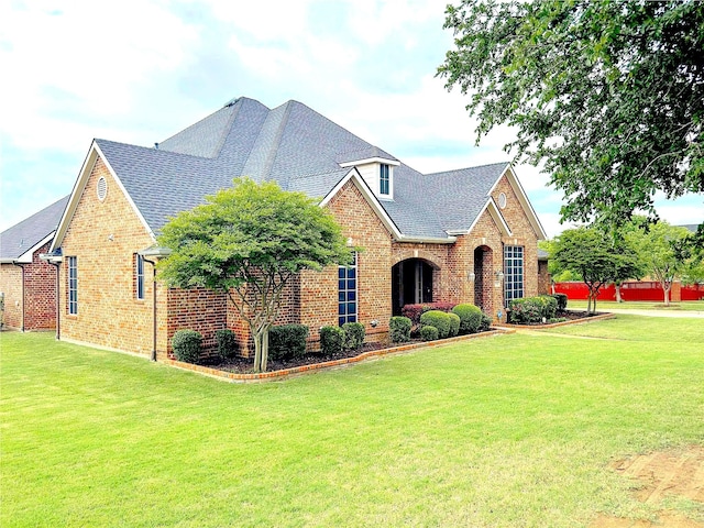 view of front facade with a shingled roof, a front yard, and brick siding