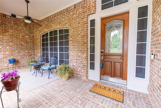 view of exterior entry featuring brick siding and a ceiling fan