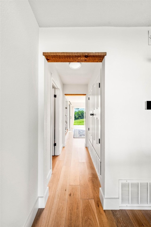 hall with visible vents, light wood-style flooring, and baseboards