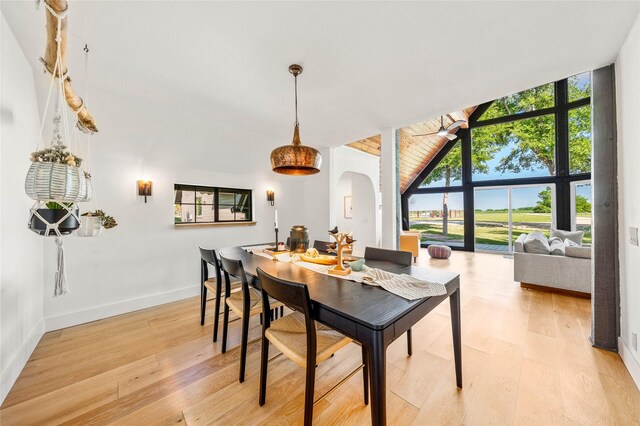 dining area featuring light wood-style floors, high vaulted ceiling, expansive windows, baseboards, and arched walkways