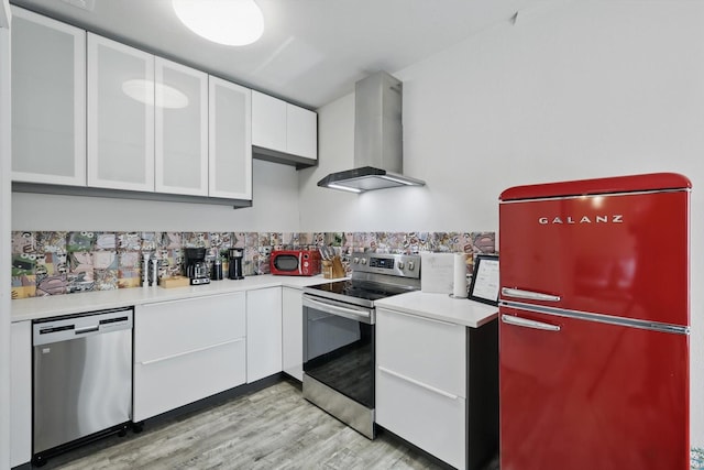 kitchen with stainless steel appliances, light wood-style flooring, wall chimney range hood, light countertops, and white cabinets