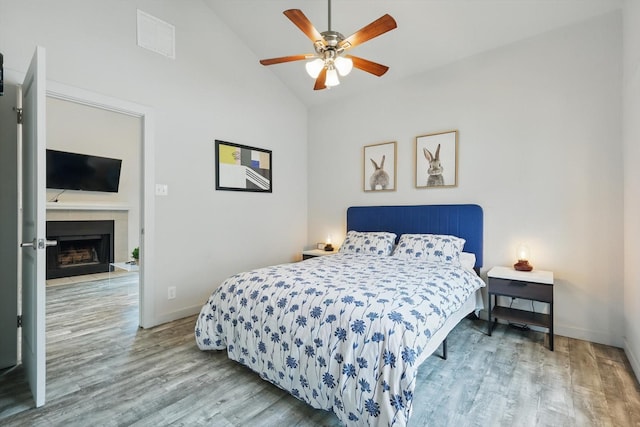 bedroom with a fireplace with flush hearth, wood finished floors, visible vents, and baseboards