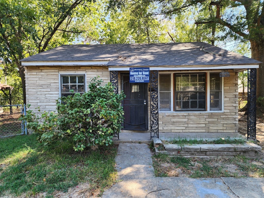 view of front of home featuring fence, stone siding, and roof with shingles