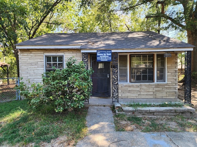 view of front of home featuring fence, stone siding, and roof with shingles