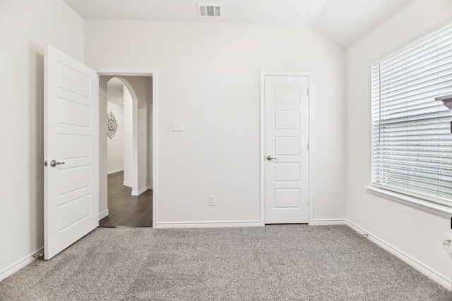 unfurnished bedroom with visible vents, arched walkways, carpet floors, baseboards, and lofted ceiling
