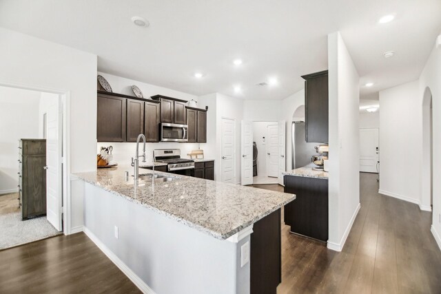 kitchen with arched walkways, appliances with stainless steel finishes, a sink, and light stone counters