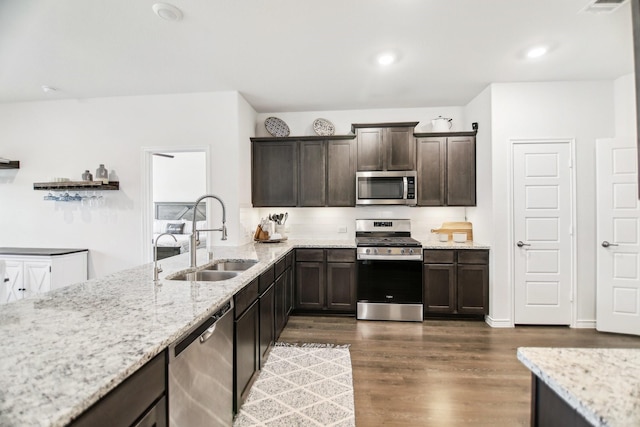 kitchen with a sink, appliances with stainless steel finishes, light stone counters, and dark brown cabinets