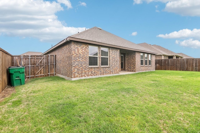 rear view of property with a fenced backyard, a yard, roof with shingles, and brick siding