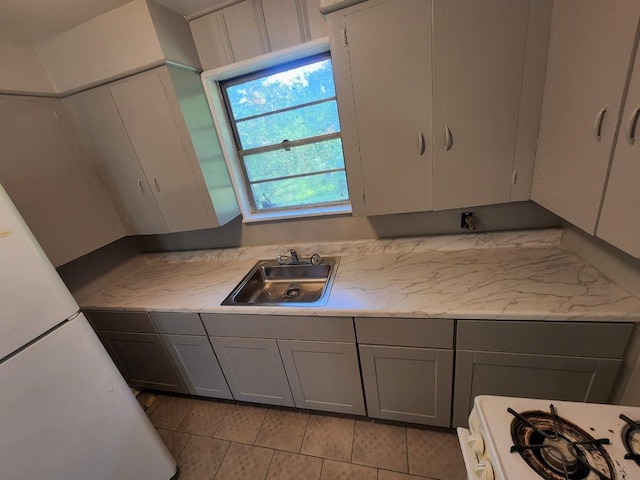 kitchen with a sink, gray cabinets, light tile patterned floors, and gas range gas stove