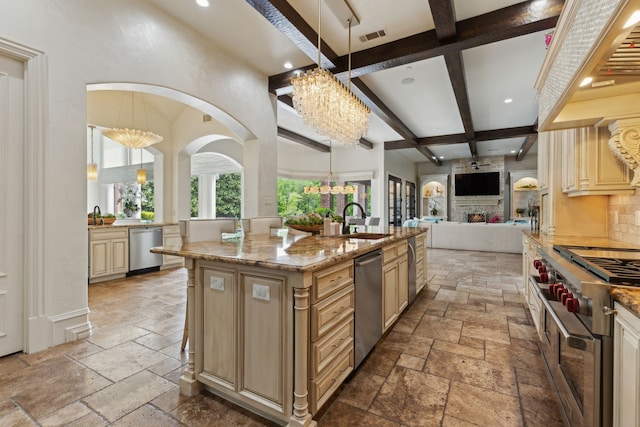 kitchen with an inviting chandelier, stainless steel appliances, stone tile flooring, a sink, and cream cabinetry