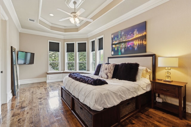 bedroom featuring a tray ceiling, crown molding, visible vents, baseboards, and wood finished floors