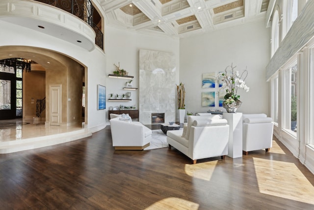 living room featuring arched walkways, dark wood-type flooring, beam ceiling, crown molding, and a towering ceiling