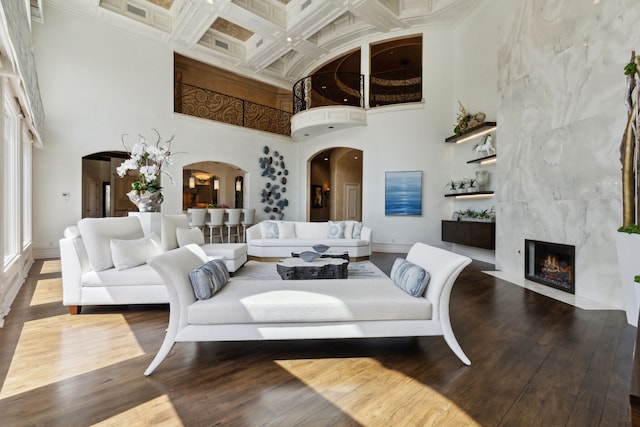 living room featuring a high ceiling, a fireplace, coffered ceiling, arched walkways, and wood finished floors