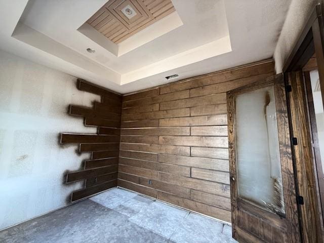 spare room featuring a raised ceiling, wooden walls, and unfinished concrete floors
