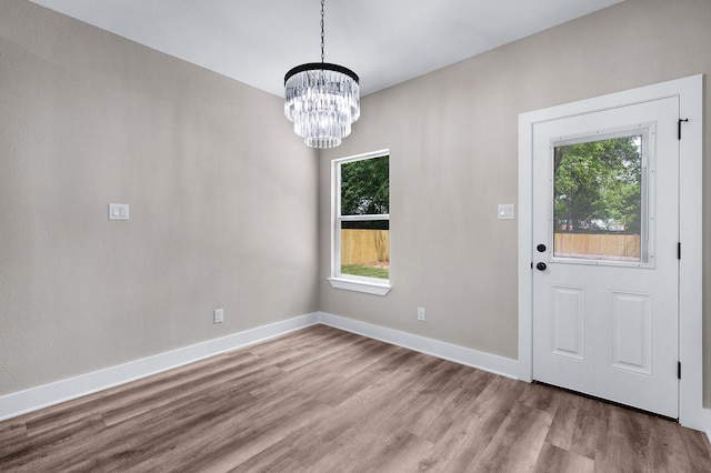 unfurnished dining area with baseboards, wood finished floors, and an inviting chandelier