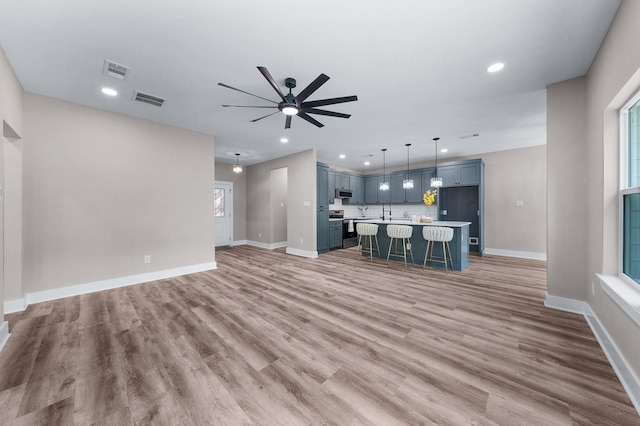 unfurnished living room featuring baseboards, visible vents, ceiling fan, and light wood-style flooring