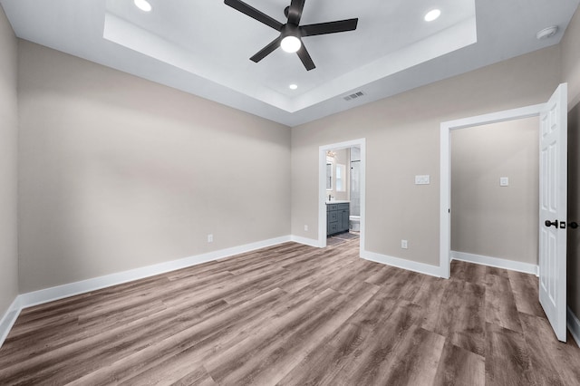 unfurnished bedroom with recessed lighting, a raised ceiling, visible vents, baseboards, and wood finished floors