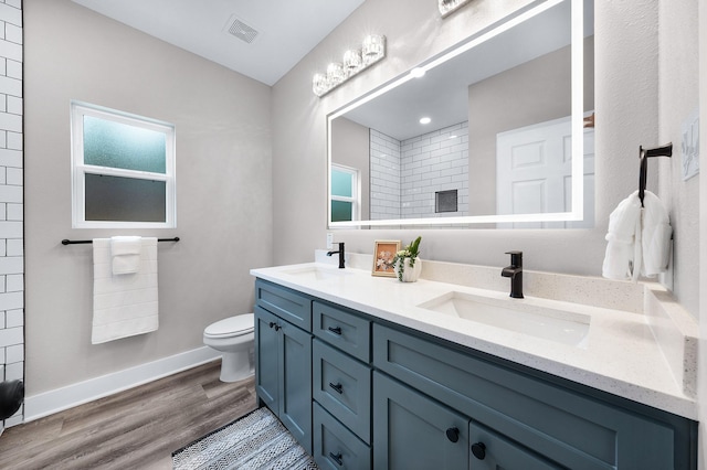 full bath with toilet, double vanity, a sink, and wood finished floors