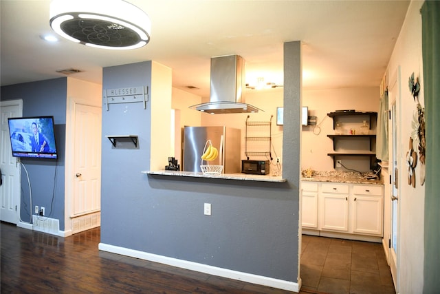 kitchen featuring freestanding refrigerator, light stone counters, white cabinetry, island range hood, and baseboards