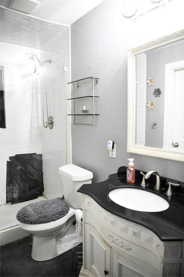 bathroom featuring vanity, toilet, visible vents, and a tile shower