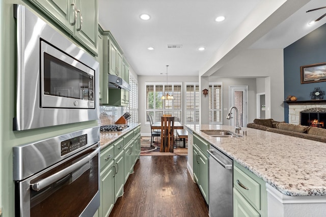 kitchen with green cabinetry, appliances with stainless steel finishes, a sink, a kitchen island with sink, and dark wood finished floors