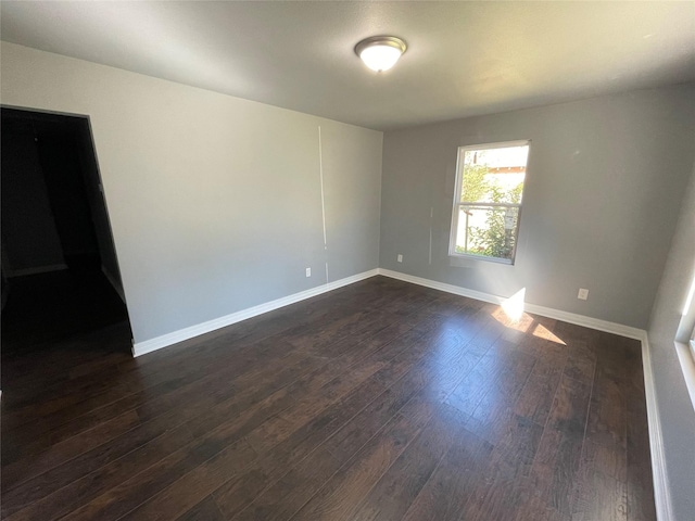 empty room with baseboards and dark wood-type flooring