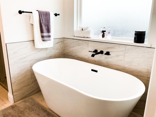 bathroom with tile walls, a soaking tub, and a wainscoted wall
