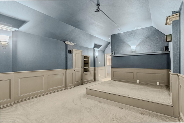 home theater room with wainscoting, carpet floors, a decorative wall, and vaulted ceiling