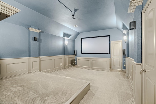 cinema featuring a decorative wall, light colored carpet, track lighting, visible vents, and vaulted ceiling