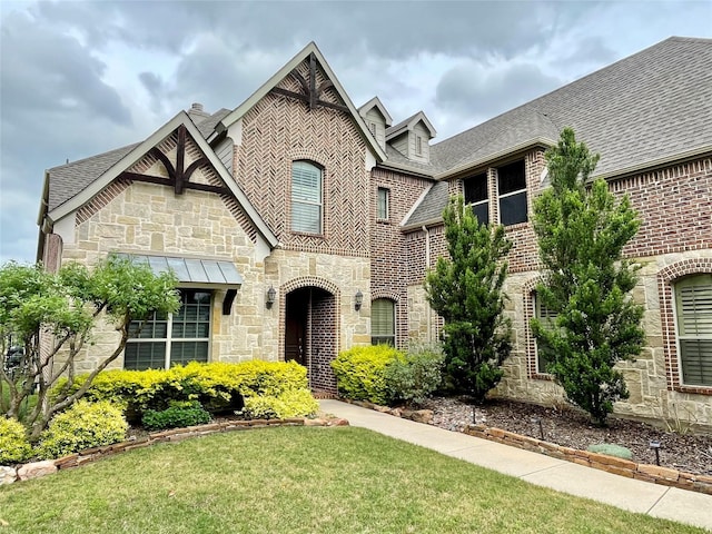 view of front of property with stone siding, a shingled roof, brick siding, and a front yard
