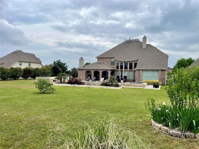 rear view of property with a yard, brick siding, a patio, and a chimney