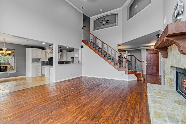 unfurnished living room featuring baseboards, ceiling fan with notable chandelier, stairs, wood finished floors, and a fireplace