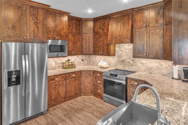 kitchen with light stone counters, decorative backsplash, stainless steel appliances, light wood finished floors, and a sink