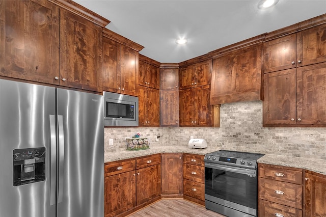 kitchen with recessed lighting, light wood-style floors, backsplash, light stone counters, and appliances with stainless steel finishes