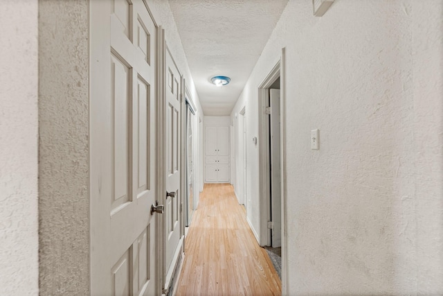 hallway with a textured ceiling, a textured wall, and light wood-style flooring