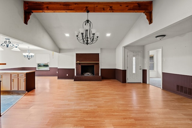 unfurnished living room featuring an inviting chandelier, light wood-style flooring, beamed ceiling, and wainscoting