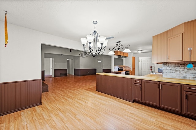 kitchen featuring an inviting chandelier, a peninsula, decorative light fixtures, light wood-style floors, and open floor plan