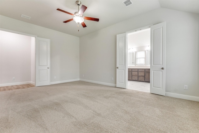 unfurnished bedroom featuring carpet flooring, baseboards, ensuite bathroom, vaulted ceiling, and visible vents