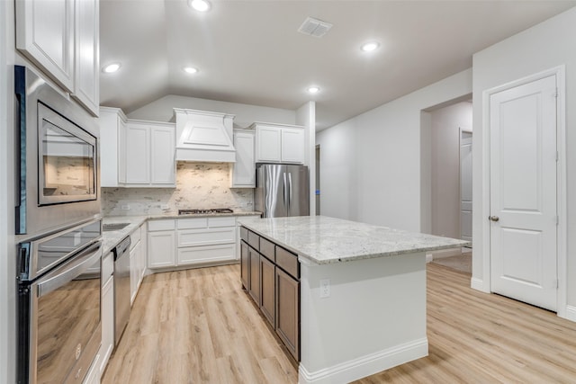 kitchen featuring appliances with stainless steel finishes, premium range hood, light wood-style flooring, and visible vents