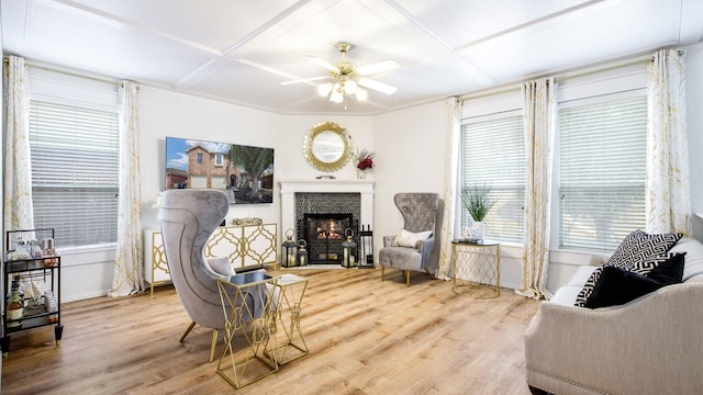 living area with wood finished floors, baseboards, ceiling fan, a lit fireplace, and coffered ceiling