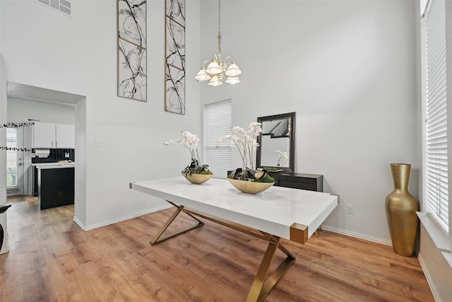 dining space with light wood-style floors, a chandelier, baseboards, a towering ceiling, and visible vents