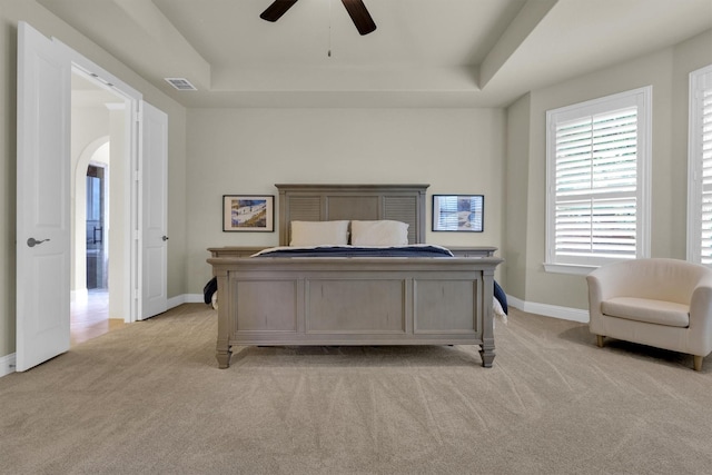 bedroom featuring light colored carpet, arched walkways, baseboards, a tray ceiling, and visible vents