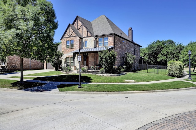tudor home with a chimney, brick siding, a front lawn, and fence