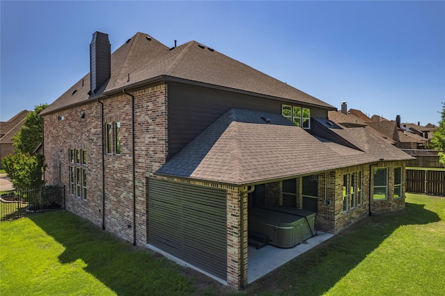 rear view of property with a hot tub, brick siding, a fenced backyard, a chimney, and a lawn