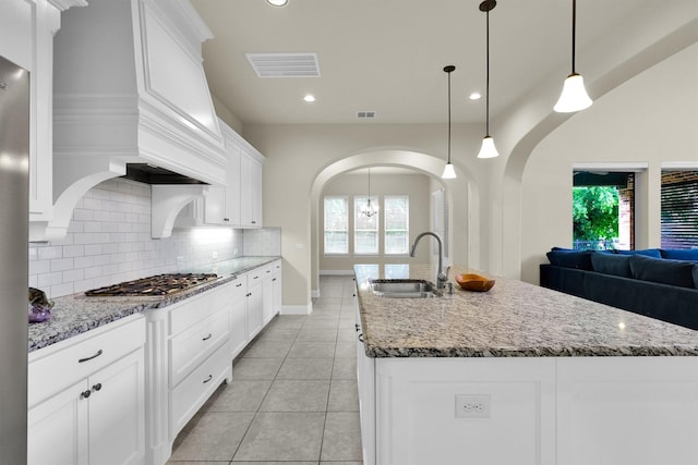 kitchen featuring visible vents, arched walkways, tasteful backsplash, a sink, and stainless steel gas stovetop