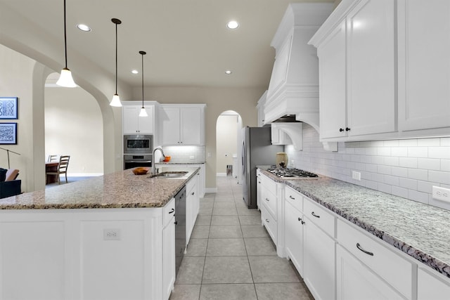 kitchen featuring a kitchen island with sink, backsplash, arched walkways, appliances with stainless steel finishes, and a sink