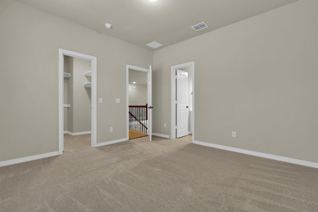 unfurnished bedroom featuring light colored carpet, baseboards, visible vents, and a walk in closet