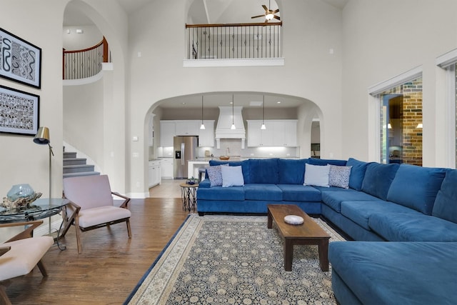 living area with a high ceiling, arched walkways, light wood-style flooring, a ceiling fan, and baseboards
